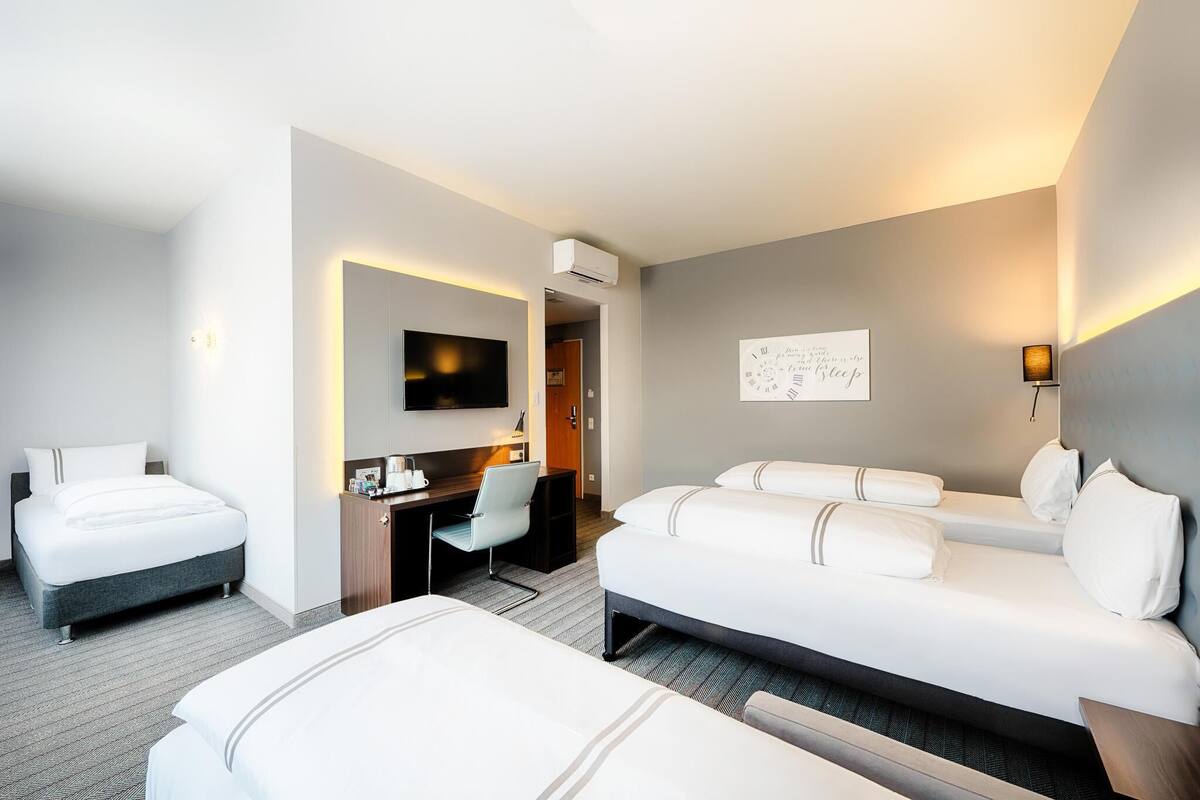 Habitación de hotel con dos camas, un escritorio, una silla, un televisor de pantalla plana y un aire acondicionado de pared.