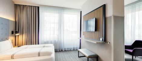 Habitación de hotel con una cama grande, un banco, un televisor en la pared y vistas a la ciudad desde las ventanas.
