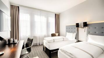 Een hotelkamer met twee bedden, een bureau met stoel, een televisie en een raam met gordijnen.