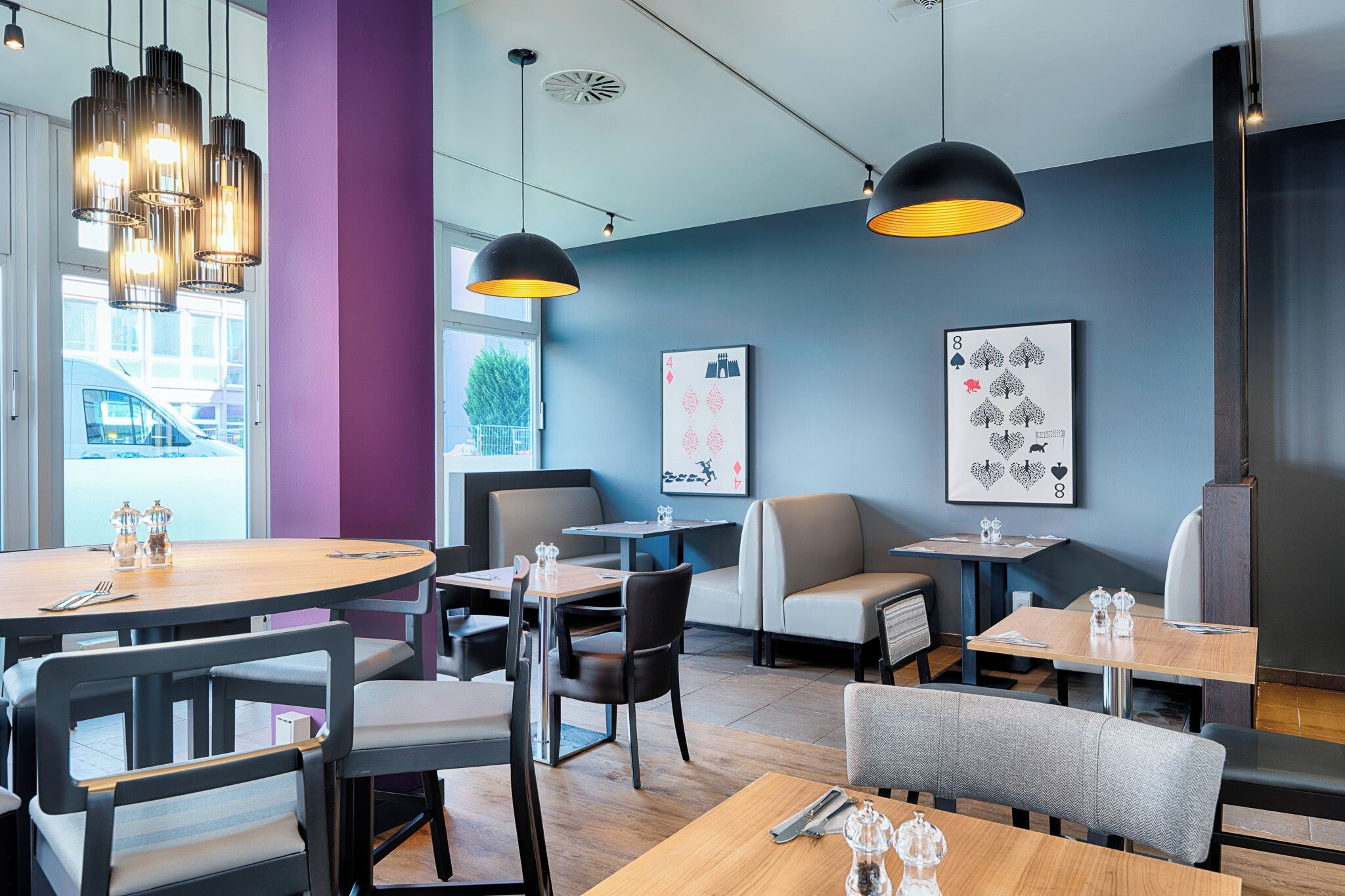 Ein modernes Restaurant mit runden Tischen, schwarzen Stühlen und Pendelleuchten.