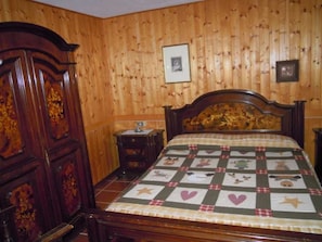 A bedroom with a wooden paneled wall, a wooden bed with a quilt, a nightstand, and a dresser.