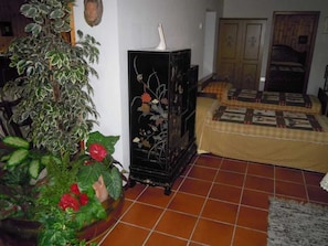 A room with a tiled floor, a bed with a patterned bedspread, a black cabinet with floral designs, and a potted plant with red flowers.