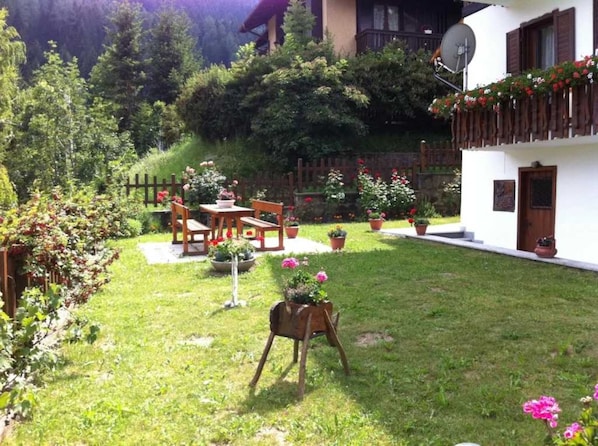 A garden with a wooden table and chairs, surrounded by potted plants and flowers.