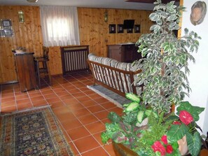 A cozy living room with a wooden floor, a patterned rug, a sofa, a coffee table, and a large potted plant with red flowers.