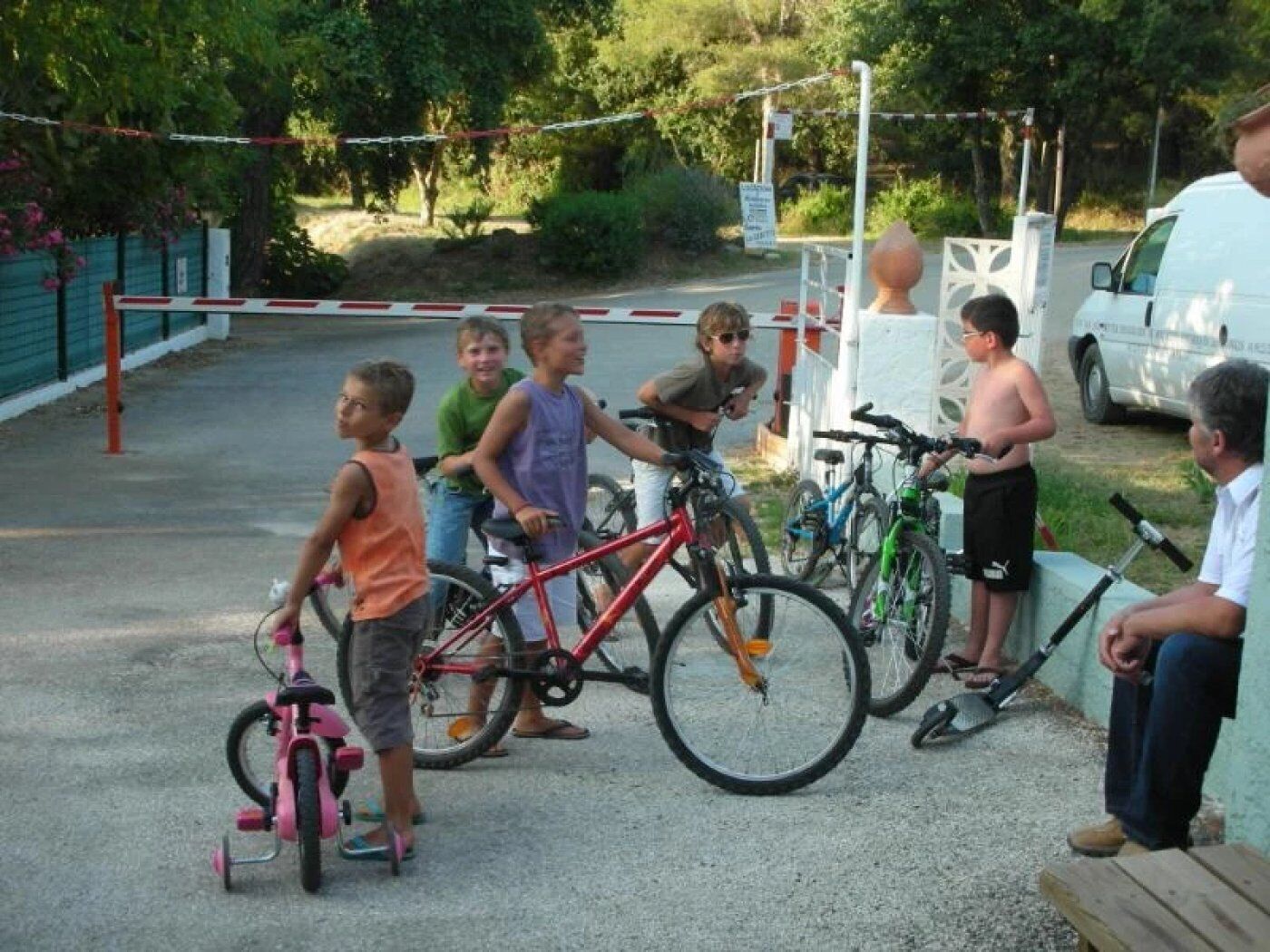 Un grupo de personas con bicicletas cerca de una zona vallada, una camioneta blanca y un edificio al fondo.