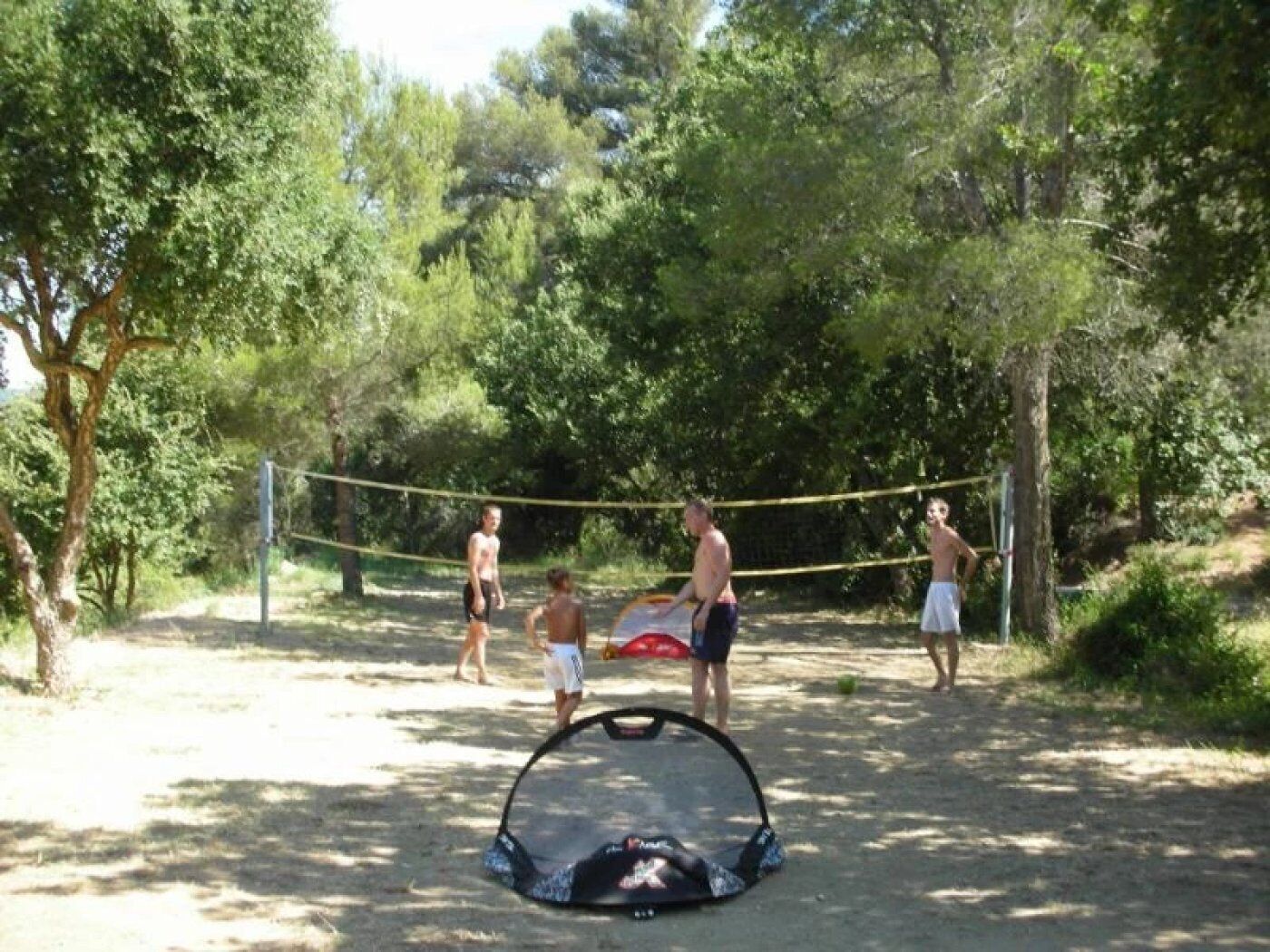 A volleyball game in a wooded area with a net and a volleyball net on the ground.