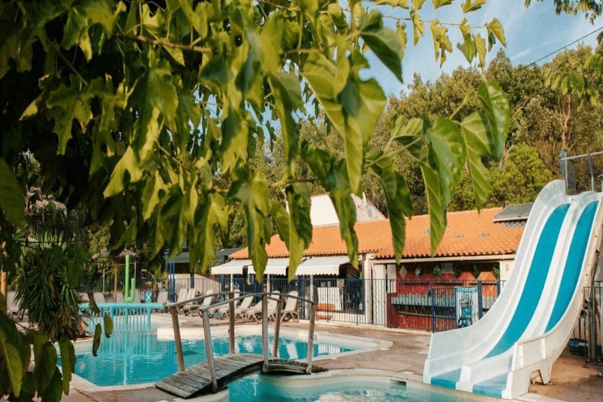 A swimming pool with a slide, surrounded by lounge chairs and a wooden deck.