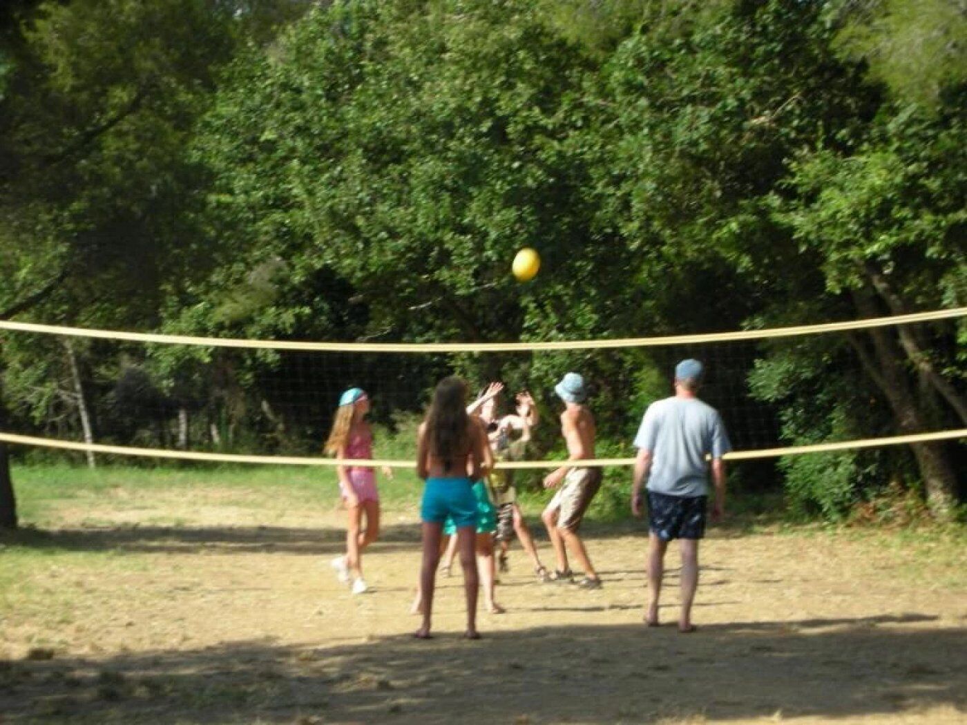 A group of people playing volleyball on a sandy court surrounded by trees.