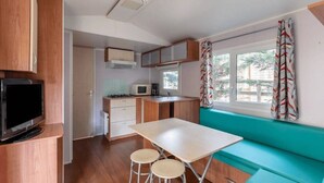 Cocina compacta con microondas, estufa y televisor. Zona de comedor pequeña con taburetes y mesa.
