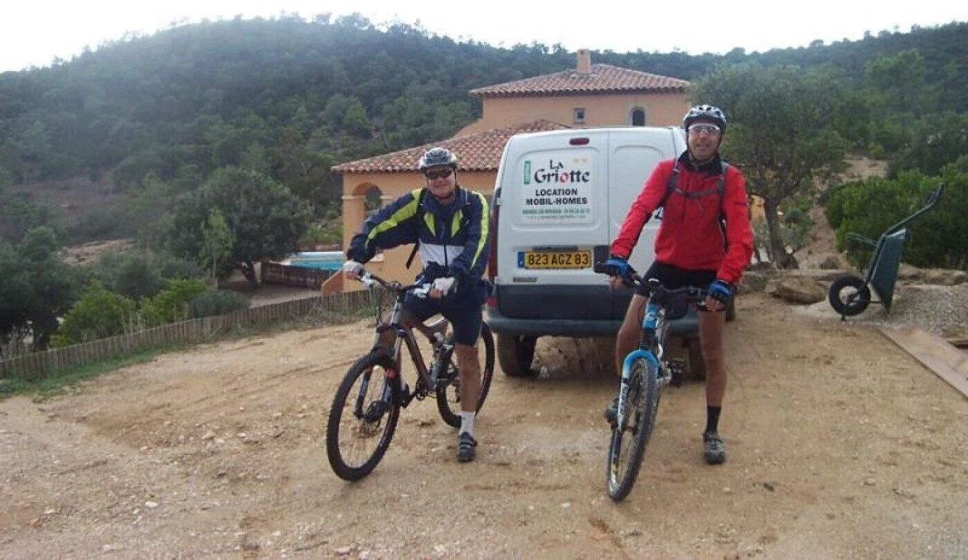 Two people on bicycles in front of a building with a sign that reads "La Grignon Mobil Homes."