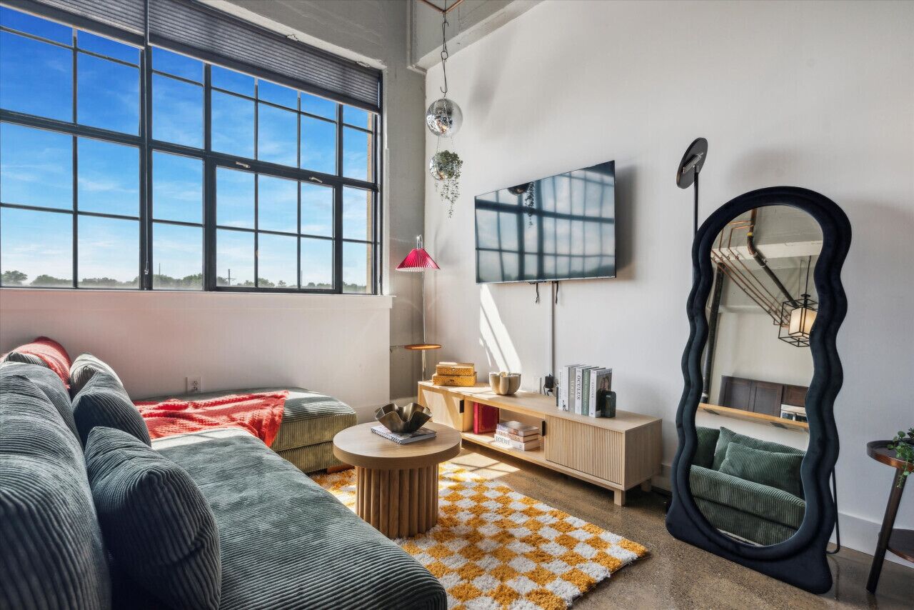 A modern living room with a large window, a sofa, a coffee table, a mirror, and a TV.
