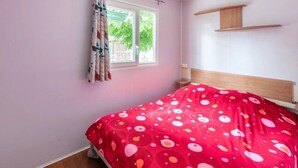 A bedroom with a bed, a window with curtains, and a wooden shelf on the wall.
