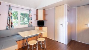 A compact kitchen with a built-in stove, a dining area with a bench and stools, and a window with curtains.