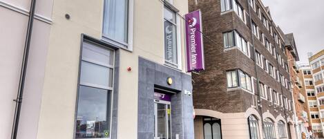 A hotel entrance with a purple sign, a glass door, and a brick building facade.