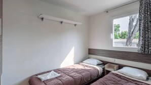 A bedroom with two single beds, a window with a view of trees, and a headboard with a light fixture.