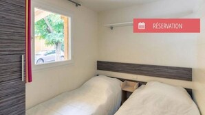 A small, single-room accommodation with two beds, a window with a view of the outside, and a 'RESERVATION' sign.