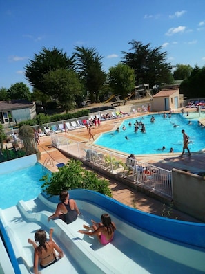 Una piscina con tobogán de agua, sillas de descanso y puesto de socorrista.