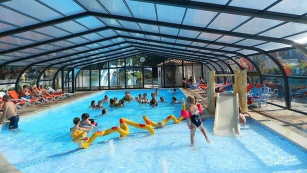 An indoor swimming pool with a covered roof, slides, and lounge areas. - ZEcamping 4* animé parc aquatique locatif TV BBQ 32m2 6 pers (Soullans)