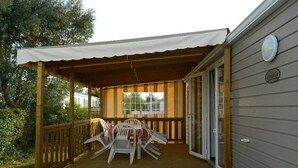 A covered outdoor deck with a table and chairs, a poolside chair, and a small table.