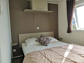 Ein Schlafzimmer mit Bett, Kopfstütze, Nachttisch, Kleiderschrank und einem Fenster mit Vorhängen.