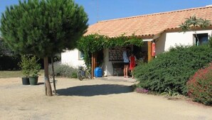 A building with a tiled roof, a small porch, and a tree in the foreground. - ZEcamping 4* familial parc aquatique animaux acceptés locatif TV BBQ (Soullans)