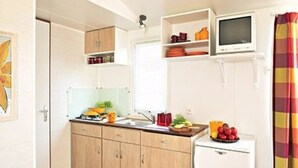 Une cuisine compacte avec des meubles de rangement en bois, un petit réfrigérateur, un four à micro-ondes et un téléviseur placé au-dessus du plan de travail.