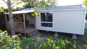 A single-story mobile home with a covered porch, a window, and a small deck area. - Camping 4 étoiles - Piscine  - efchaa (Bourgneuf-en-Retz)