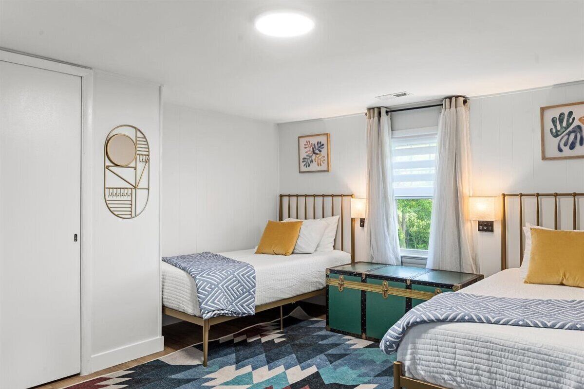 A room with two beds, a window with curtains, and a wall-mounted artwork.