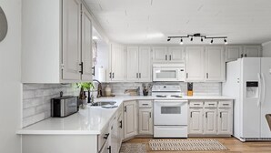Une cuisine moderne avec des meubles blancs, un four à micro-ondes encastré, une cuisinière et un réfrigérateur.