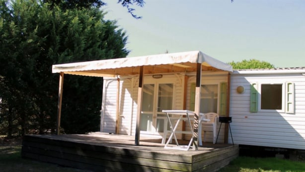 A mobile home with a covered patio area, a small table, and a chair. - ZEcamping 4* animé piscine couverte mobil-home TV BBQ 30m2 6 pers (Bourgneuf-en-Retz)