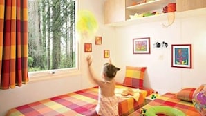 A child's room with two beds, colorful bedding, a window with curtains, and various toys and decorations. - ZEcamping 4* animé piscine couverte mobil-home TV BBQ 30m2 6 pers (Bourgneuf-en-Retz)