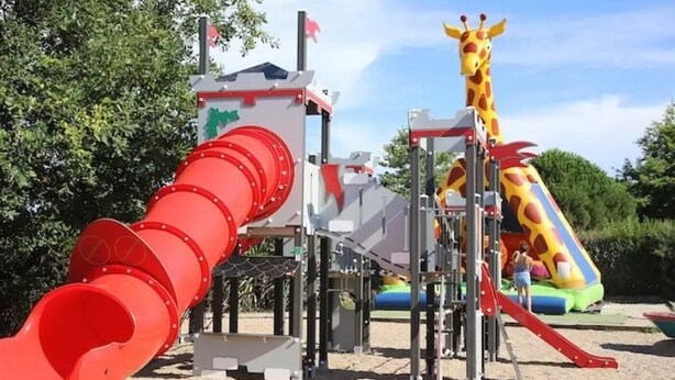 A playground with a red slide, a giraffe-shaped slide, and a play structure.