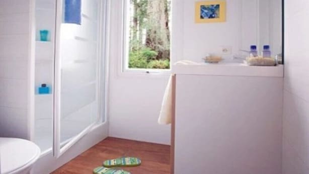 Ein kleines Badezimmer mit Dusche, Toilette und einem Fenster mit Blick auf Bäume.