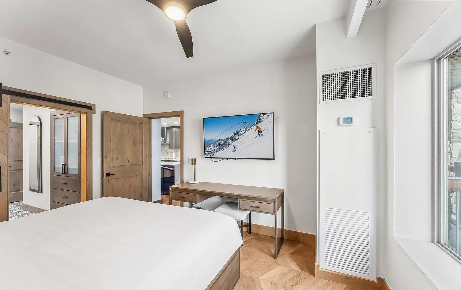 A modern bedroom with a bed, desk, and a large window.