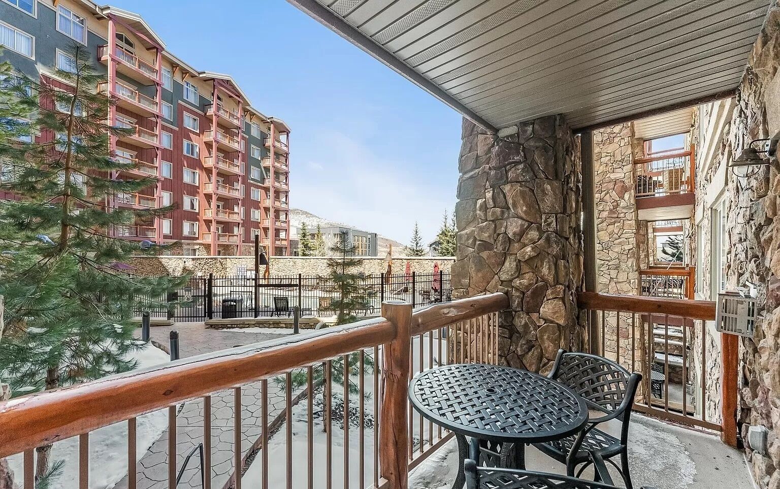 A balcony with a stone wall, a metal railing, and a table with chairs.