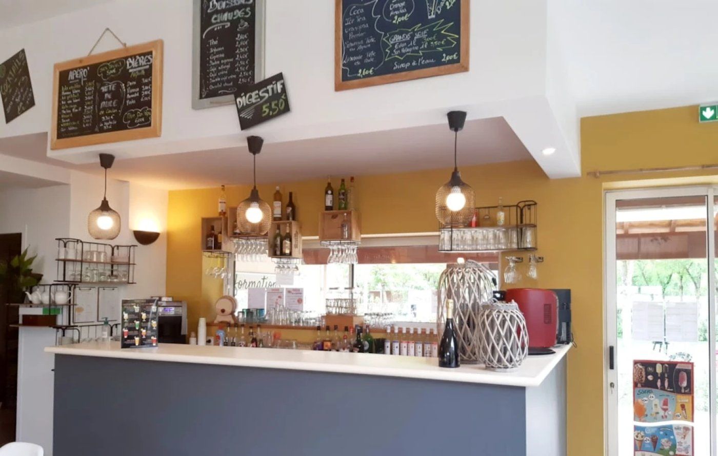 A bar area with a counter, hanging lights, and various bottles and glasses.