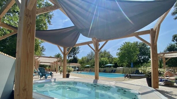 A wooden deck with a hot tub, surrounded by lounge chairs and umbrellas, under a shaded pergola. - ZEcamping 4 étoiles animé pataugeoire tente TV 29m2 5 pers (Coulon)