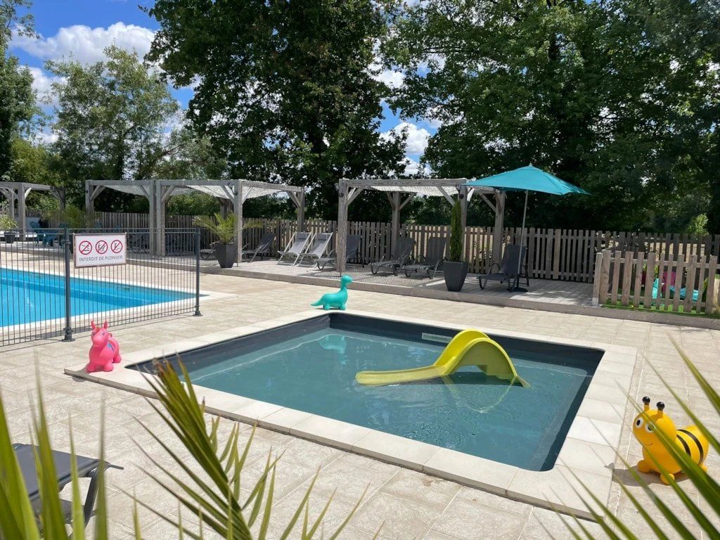 A swimming pool with a slide, lounge chairs, and a fenced area with a pergola.