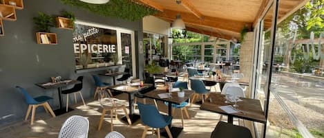 Een terras met tafels en stoelen, een zichtbaar restaurantsbord en uitzicht op de straat.