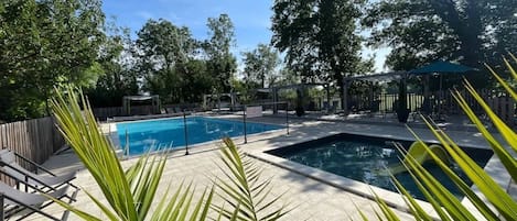 A pool area with a clear blue pool, a smaller hot tub, and lounge chairs.