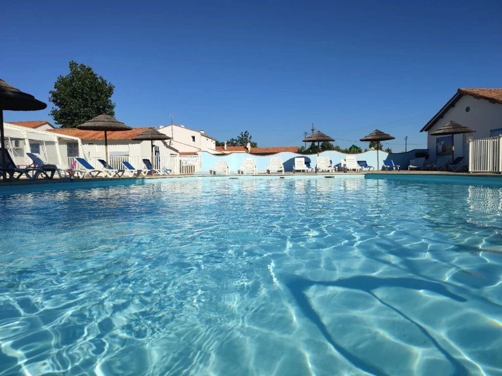 A clear swimming pool with lounge chairs and umbrellas, surrounded by buildings with a consistent architectural style.