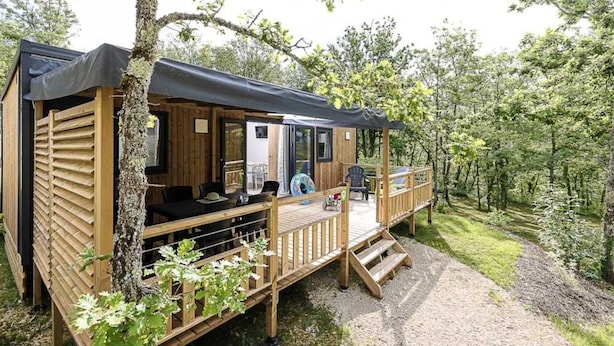 A wooden cabin with a deck, a covered outdoor seating area, and a gravel path. - ZEcamping 4 étoiles animé parc aquatique mobil-home TV LV BBQ 32m2 (Loupiac)