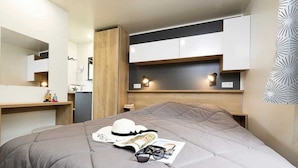 A modern bedroom with a grey bed, wooden headboard, and built-in storage cabinets. - ZEcamping 4 étoiles animé parc aquatique mobil-home TV LV BBQ 32m2 (Loupiac)