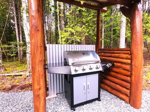 En bærbar grill står klar i en træpavillon i et skovområde.