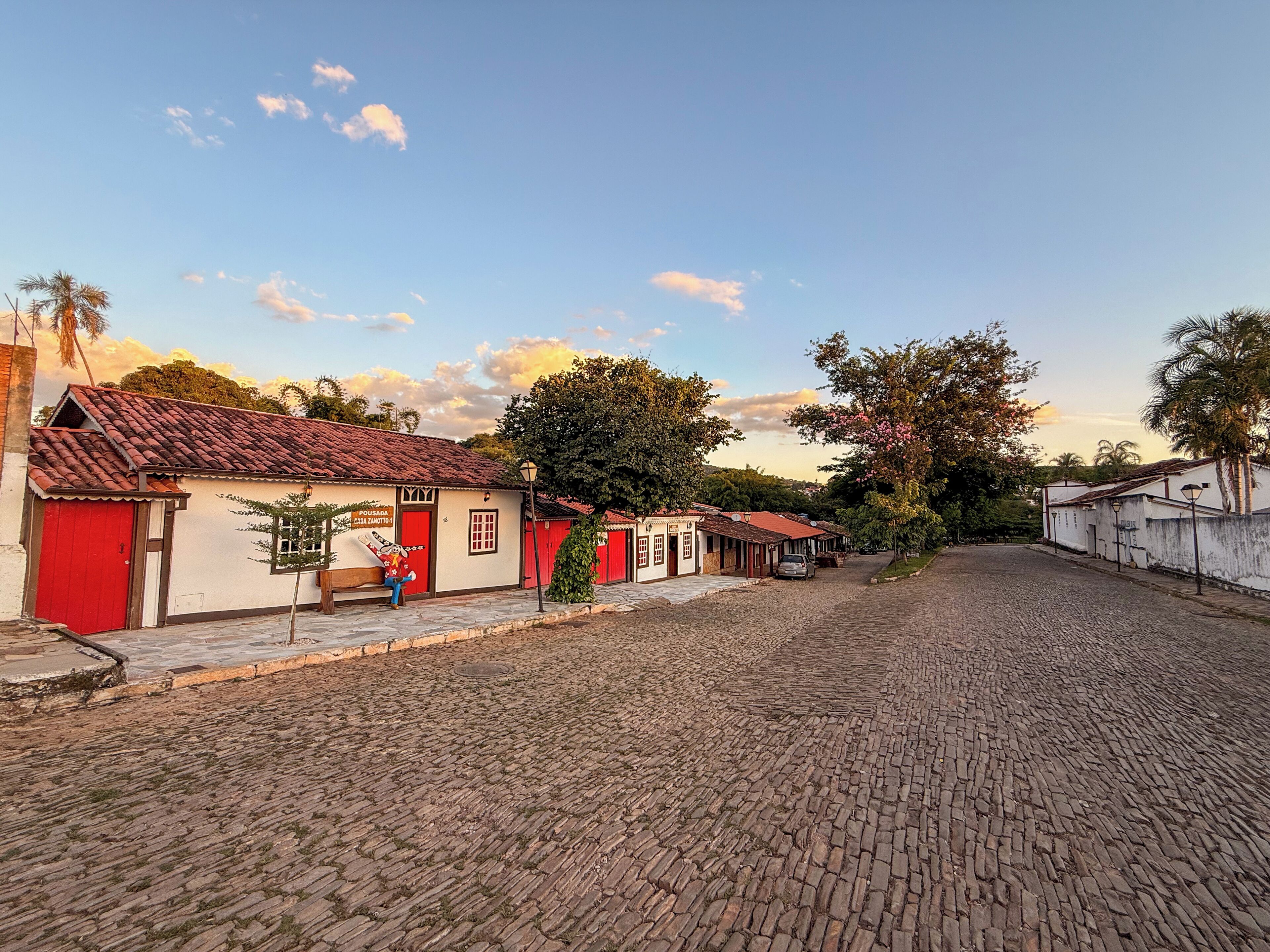 A cobblestone street lined with traditional buildings, some with red doors, and a clear sky.