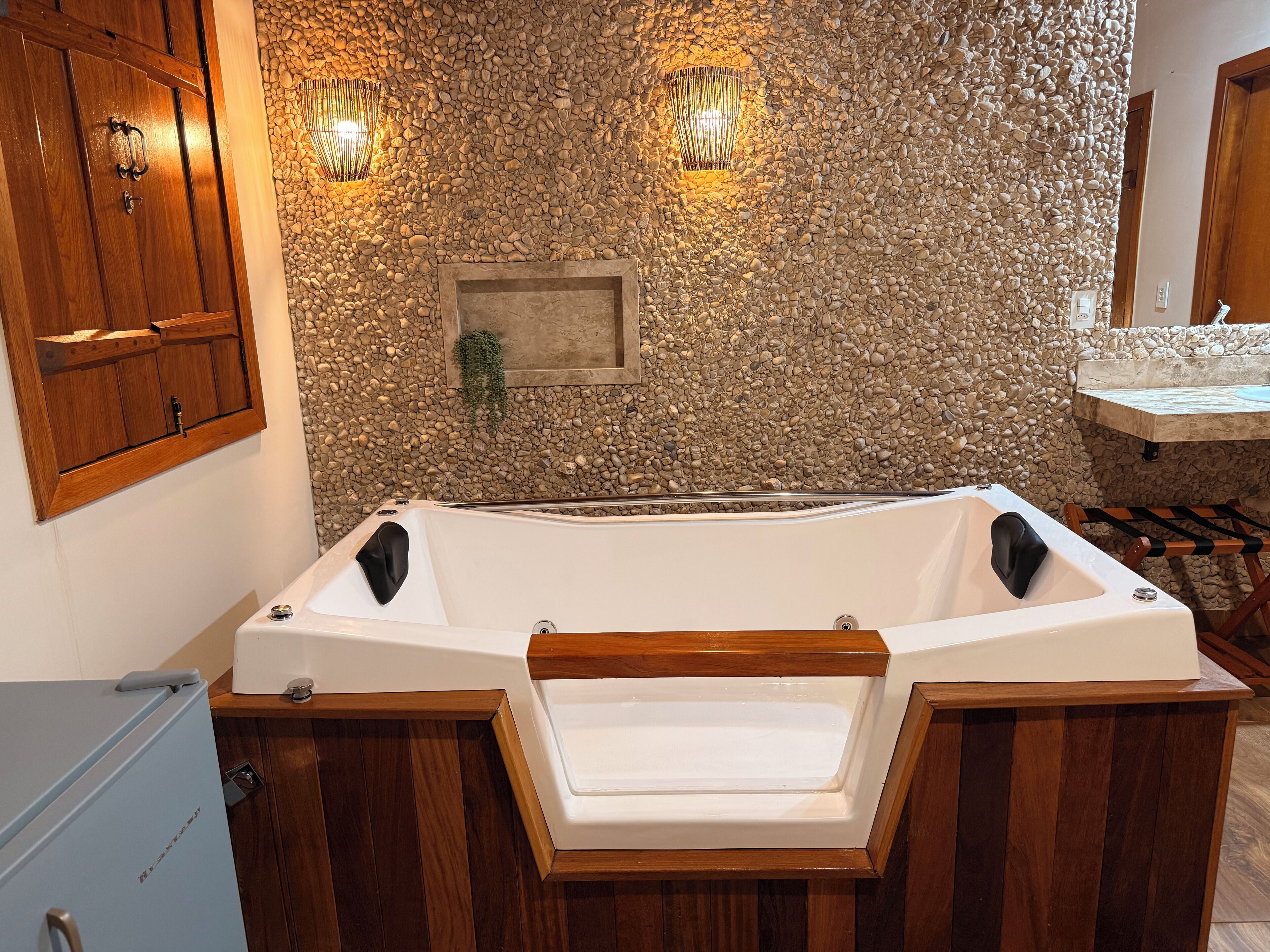 Un baño con pared de piedra, una bañera, armarios de madera y dos luces empotradas.