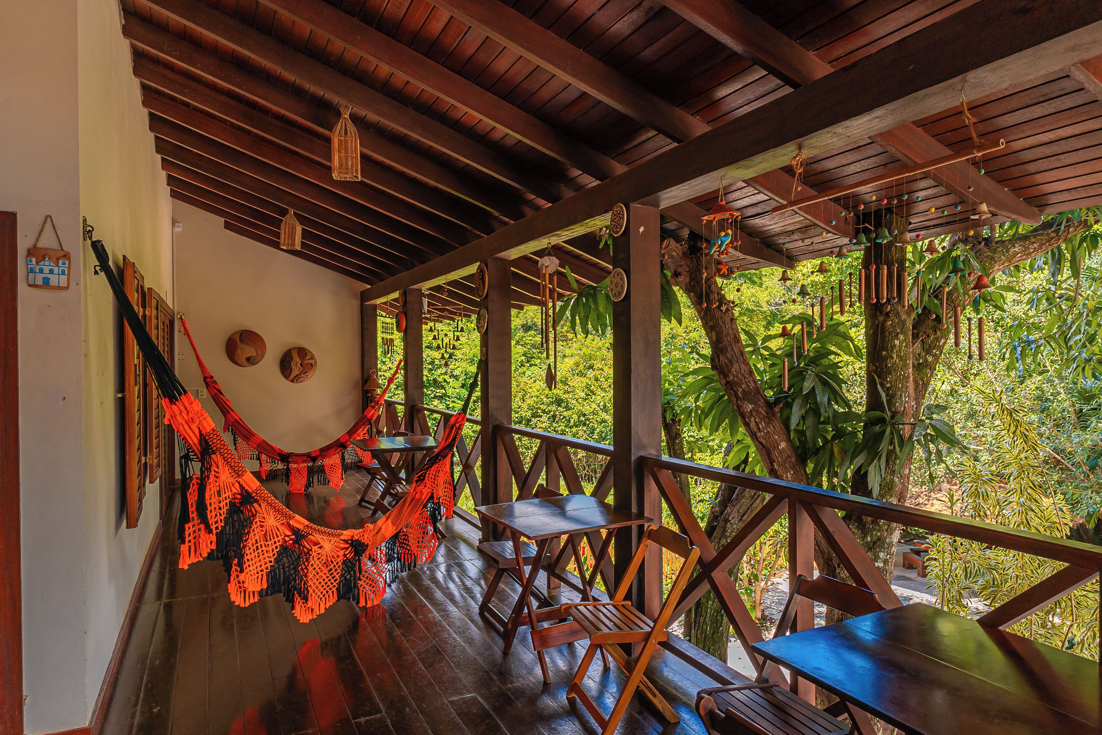 A wooden deck with tables and chairs, a hammock, and a view of lush greenery.