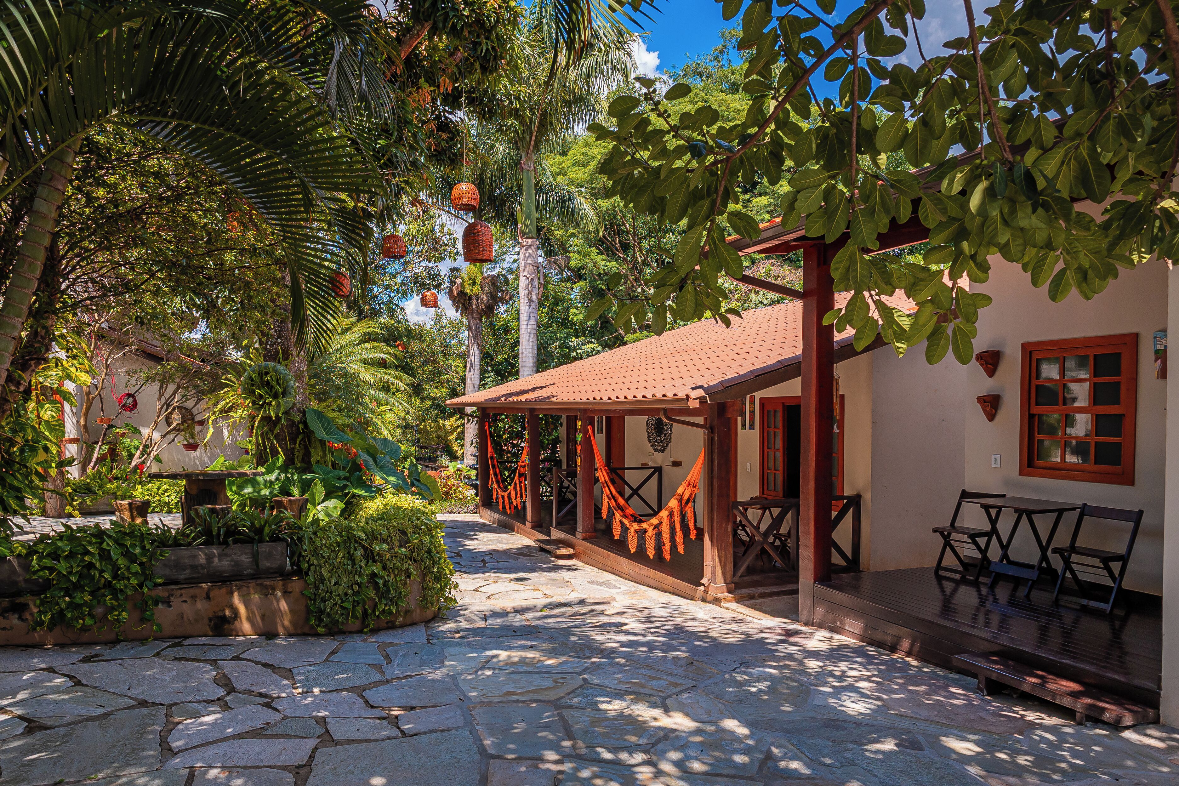 A courtyard with stone flooring, a covered seating area, and lush greenery.
