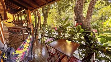 A wooden deck with a table and chairs, surrounded by trees and a hammock.
