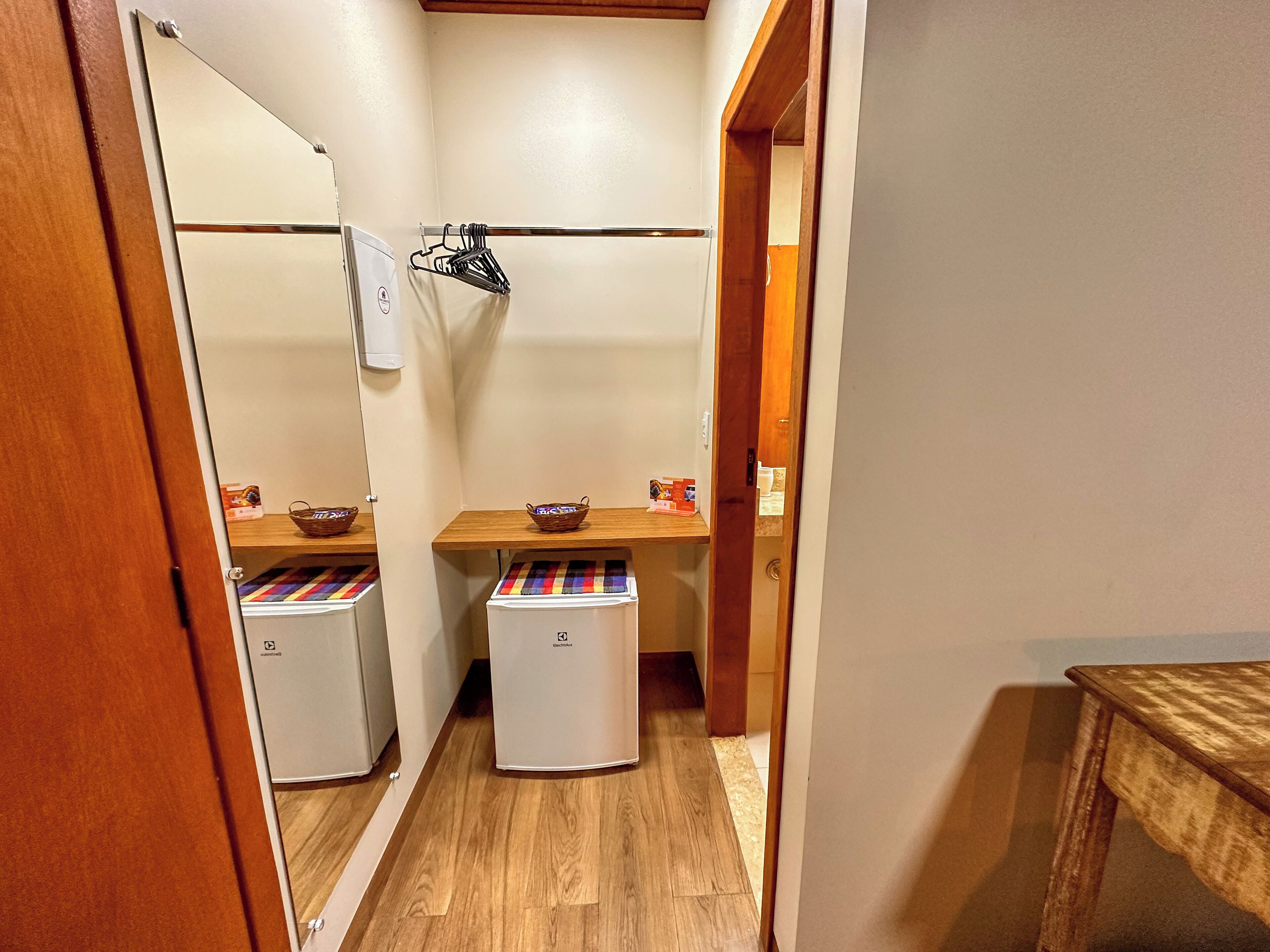 A narrow hallway with a wooden floor leading to a bathroom. There are two sinks with wooden countertops and a mirror above them. A basket and a towel rack are visible on the countertop.